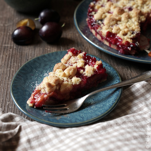 KI generiert: Ein Stück Pflaumen-Crumble-Kuchen auf einem blauen Teller, daneben eine Gabel.