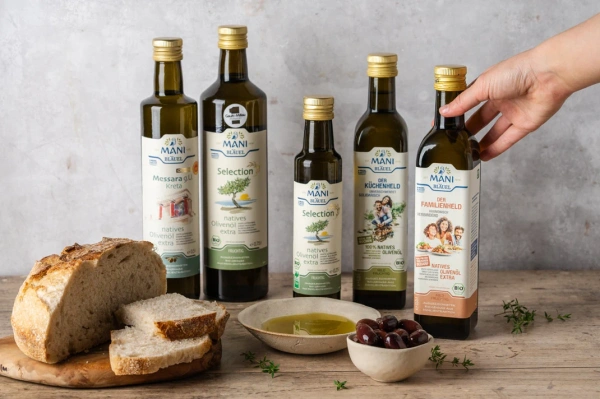 KI-generierte Beschreibung: Bild zeigt verschiedene Öle und Brot auf rustikalem Tisch. Enthält Text: "MANI Selection natives Olivenöl extra".