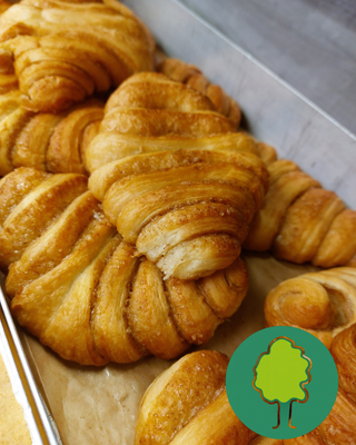 KI generiert: Knusprige Croissants auf einem Blech. Unten rechts ein grünes Baum-Logo.