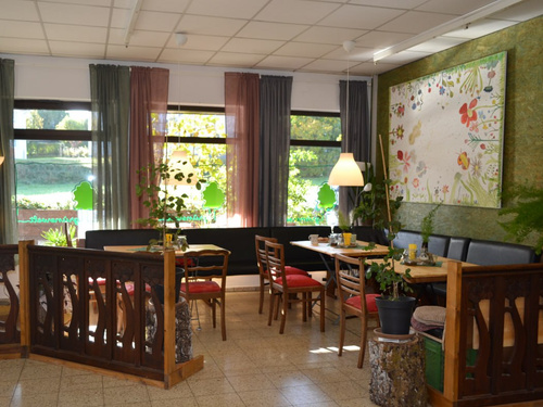 KI generiert: Ein gemütliches Café mit Holzmöbeln, Pflanzen und bunter Wanddekoration.