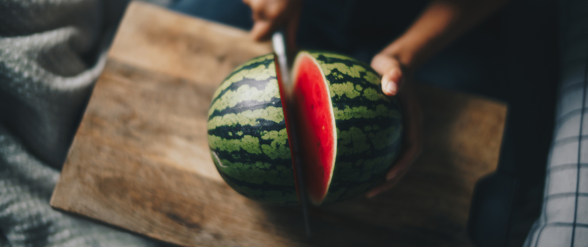 KI generiert: Eine Person schneidet eine Wassermelone auf einem Holzbrett.
