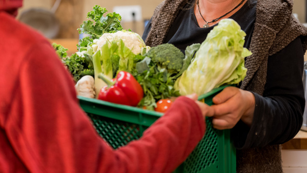 KI generiert: Zwei Personen tauschen einen Korb voller frischem Gemüse aus, darunter Paprika, Blumenkohl und Salat.