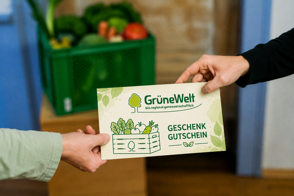 KI generiert: Zwei Personen tauschen einen "GrüneWelt"-Geschenkgutschein. Im Hintergrund ist eine Kiste mit Gemüse.