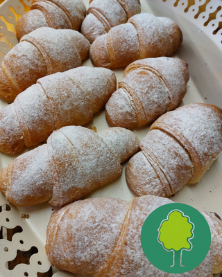 KI generiert: Acht frisch gebackene Croissants mit Puderzucker bestäubt auf Tablett, Logo eines Baumes unten rechts.