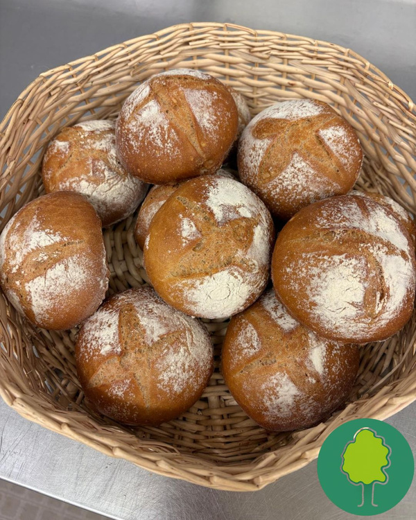 KI generiert: Ein Korb mit frischen, bemehlten Brötchen. Unten rechts ein Baum-Icon.