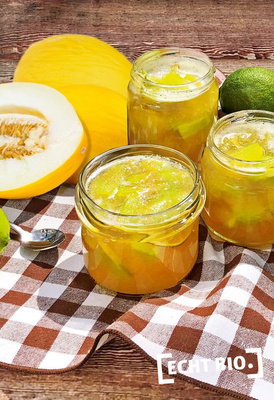 KI generiert: Gläser mit gelber Marmelade, Melonen und Limetten auf kariertem Tuch. Text: "ECHT BIO."