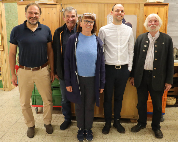 KI generiert: Fünf Personen lächeln in die Kamera; sie stehen vor einem Holzschrank. Text ist teilweise sichtbar.